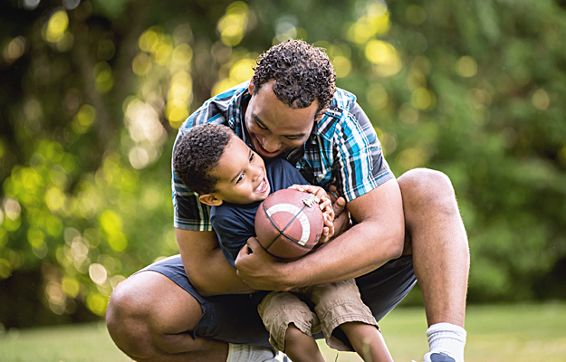 A father and his young son playing football together.