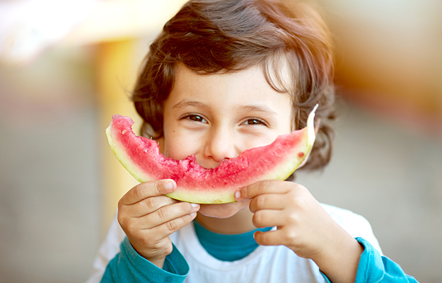 A toddler holding a slice of watermelon over his mouth.