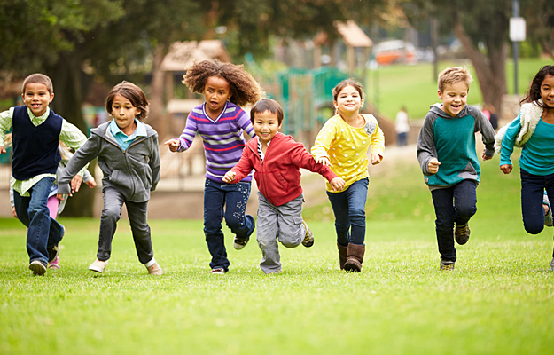 A group of children running over playground grass.