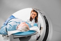Graphic of health practician overlooking elderly man laying down on hospital bed about to get a CT scan, associated with July 2019 research spotlight article on 'Nudges to change palliative care'.