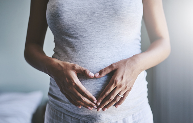 A woman's hands forming the shape of a heart over her pregnant stomach.