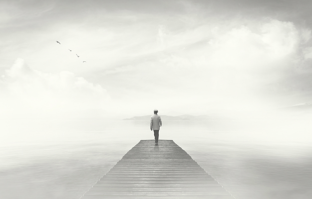 A dream-like photo of a man reaching the end of a boardwalk in heavy fog.