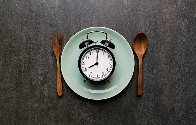 An alarm clock on a dinner plate with eating utensils placed on the sides.