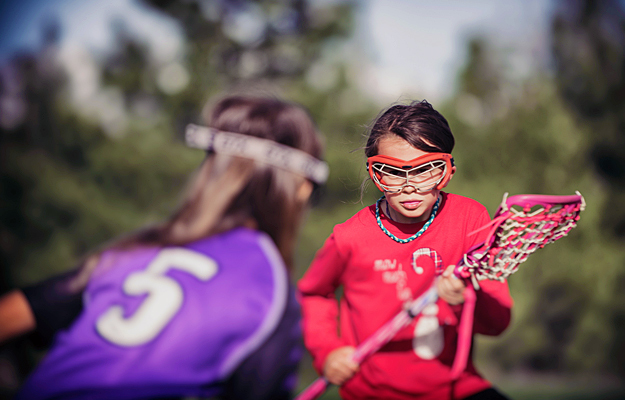 Two young girls playing lacrosse and wearing protective eyewear.