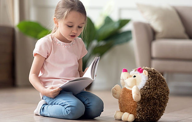 A young girl reading to her stuffed animal.
