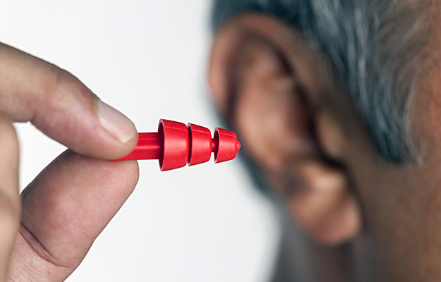 A closeup of a man holding a pre-molded earplug in front of his ear.