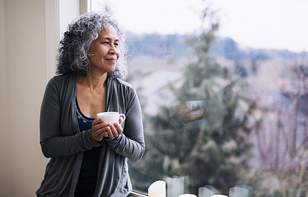 A senior woman drinking tea and looking out a window.