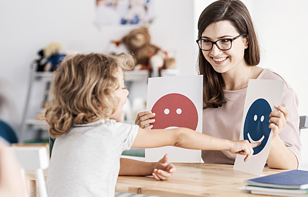 An adult showing a child flashcards with pictures of different faces.