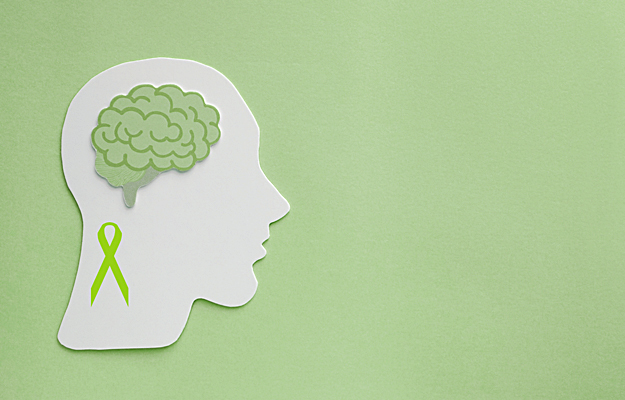 Paper cutouts of a green awareness ribbon and brain on a green background.