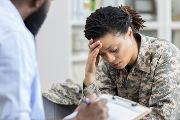 Female military veteran holding her head in an appointment with a health professional
