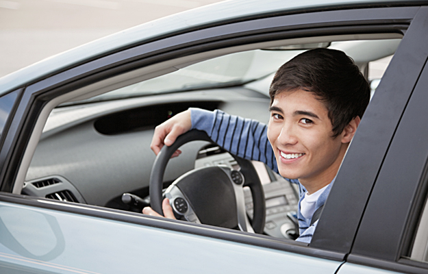 A teenage boy sitting in the driver seat of a car.