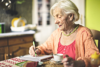 Senior woman in the kitchen writing in a notebook