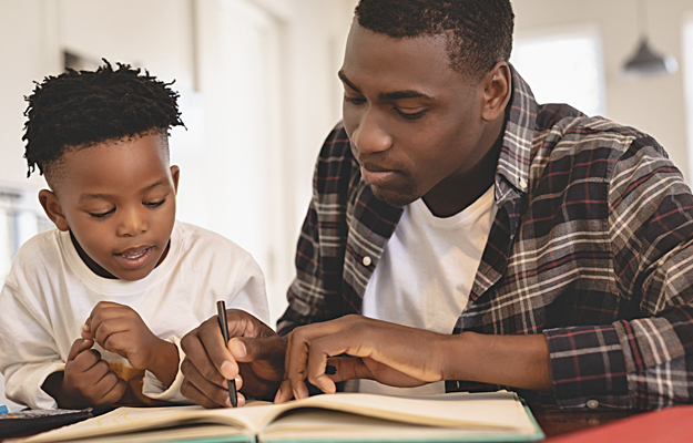 An African American father and son working on an activity book together.