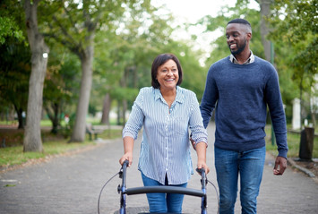 Mature woman using walker with young man assisting