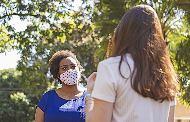 A woman in a cloth face mask having a socially distanced conversation with someone.