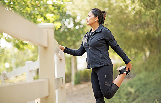 A mature woman stretching her legs outside before exercising. 