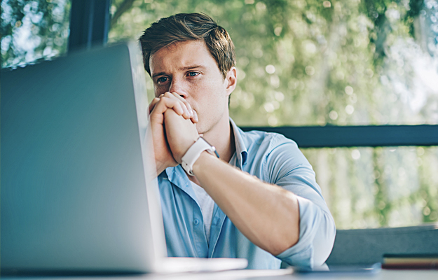 A young man looking pensively at a laptop.