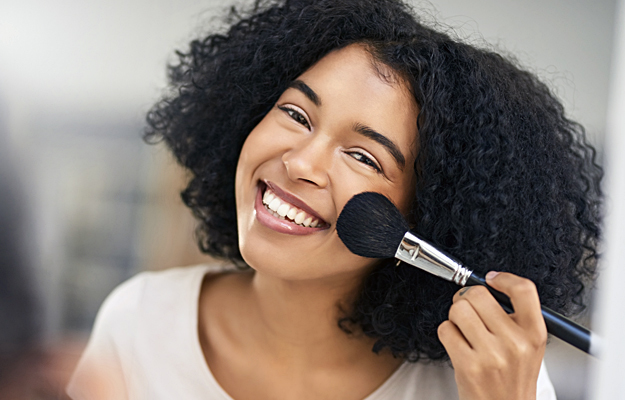 A woman applying blush to her cheek.