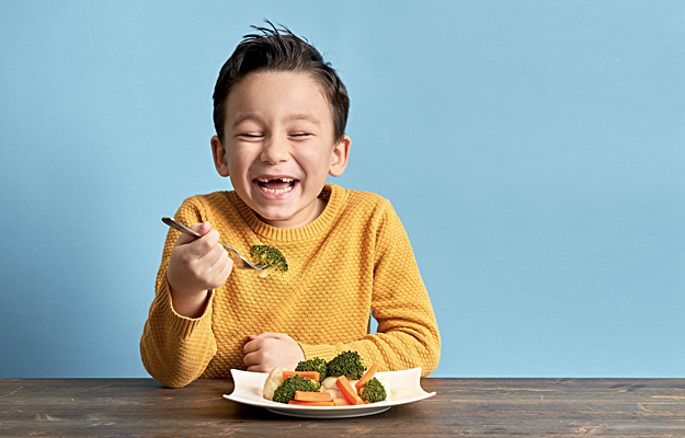 A smiling young boy eating a plate of vegetables.