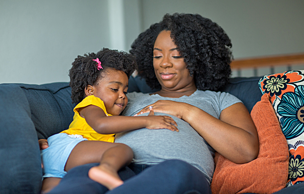 A pregnant woman and her young daughter touching and looking at her stomach.