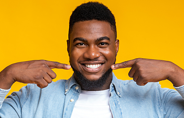 A smiling young man pointing to his mouth.