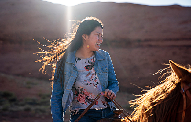 A teenage Navajo girl riding a horse.