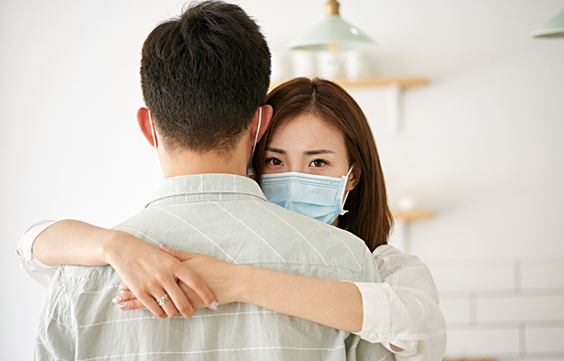 A young woman with a face mask on hugging a man.