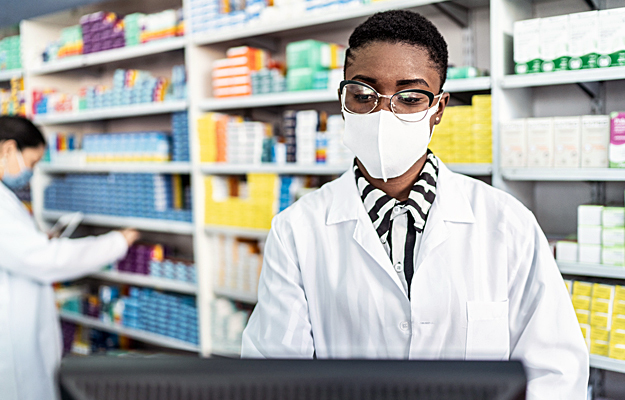 A female pharmacist wearing a face mask looking at a computer.