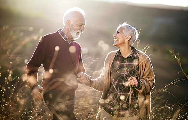A cheerful senior couple walking through tall grass.