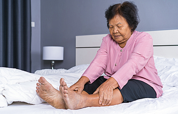 A senior woman sitting in bed and holding her legs.