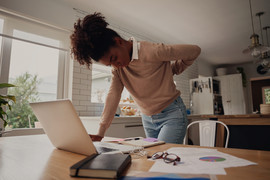 Young woman standing and holding back while working on laptop at home