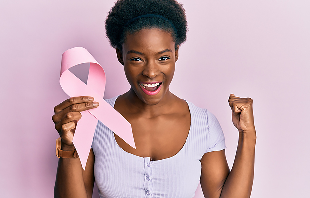 A woman holding a pink awareness ribbon with one hand and making a fist with the other. 