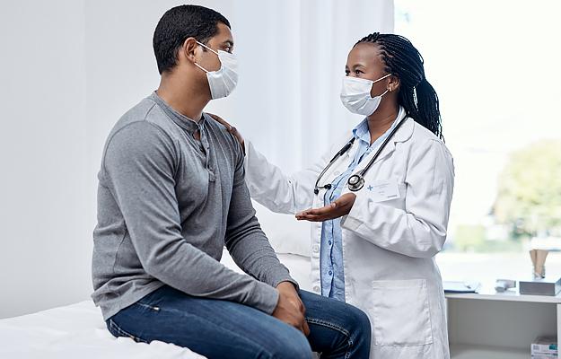 A masked man talking with a masked doctor.