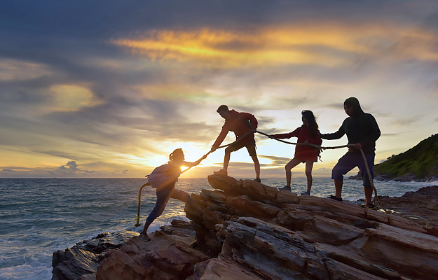 A group of people helping a person climb up a rock.