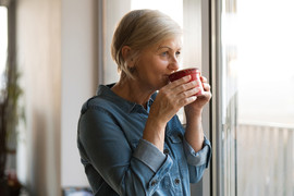 Senior woman looking out a window sipping a cup of tea