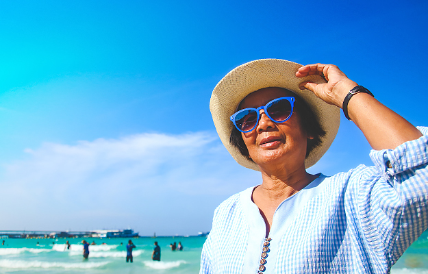 A senior woman wearing sunglasses and a hat on the beach.