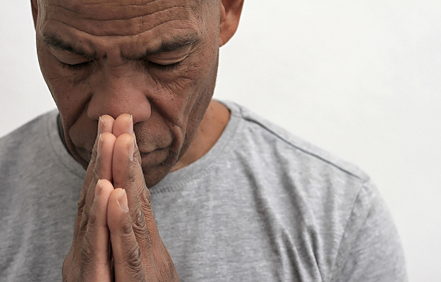A mature black man with his hands together in thought or prayer.