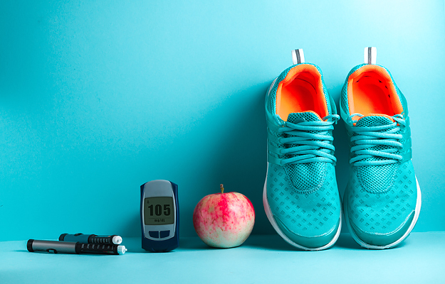 Insulin pens, a blood glucose monitor, an apple, and running shoes on a blue background.
