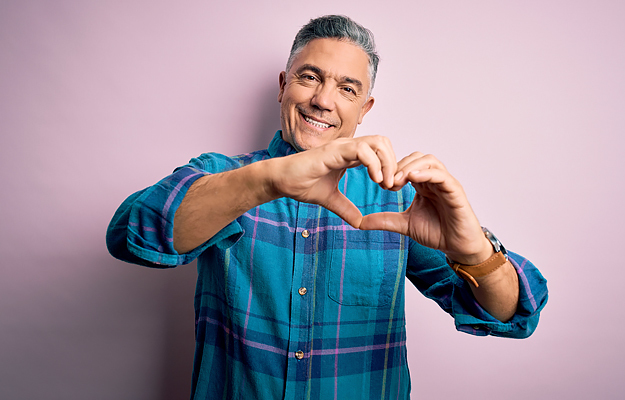 A mature man forming the shape of a heart with his hands.