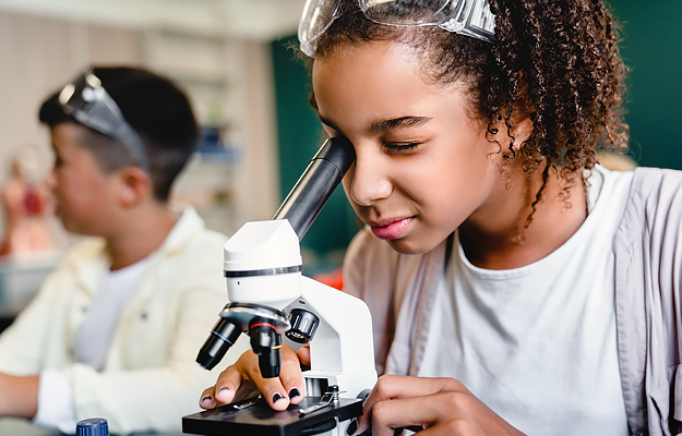 A teenage girl looking into a microscope.