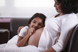 Young girl with her ear against a woman's pregnant belly