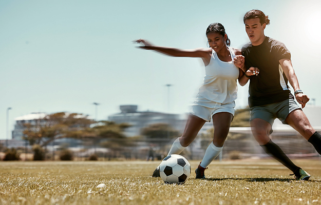 Two young adults playing soccer outdoors.