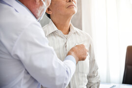 Doctor listening to older patients chest with stethoscope.