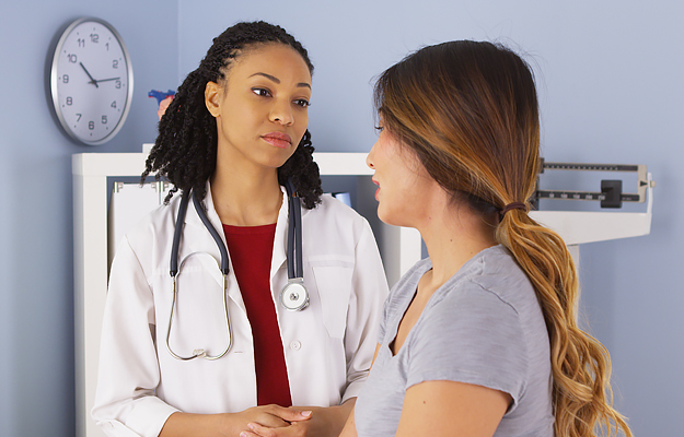 A doctor talking to a young female patient in an exam room.