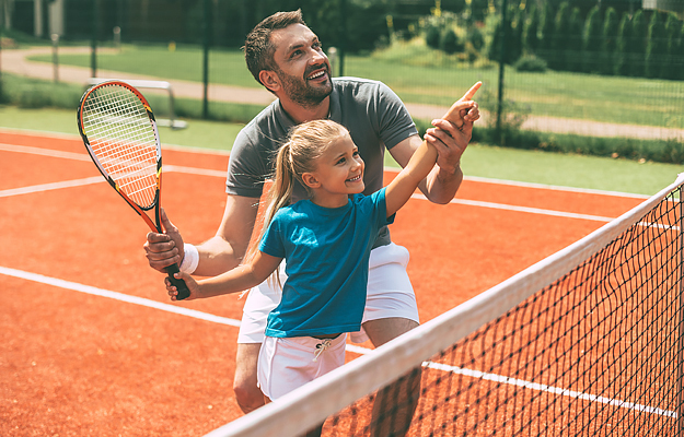 A man and his young daughter playing tennis.