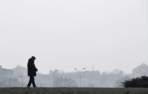 A silhouette of a senior man walking alone outside a city on a hazy, polluted day.