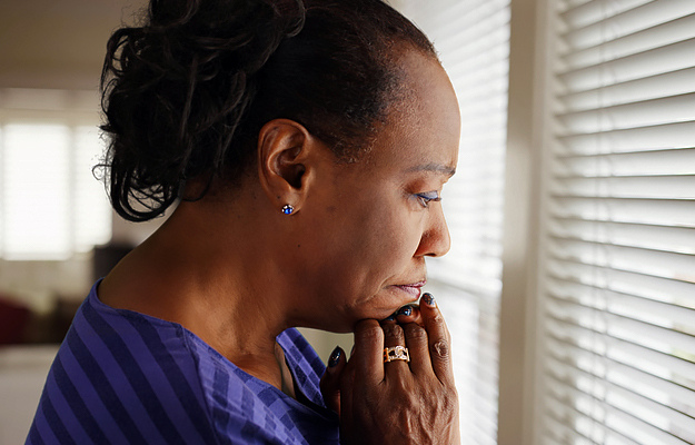 A mature woman mournfully looking out a window.