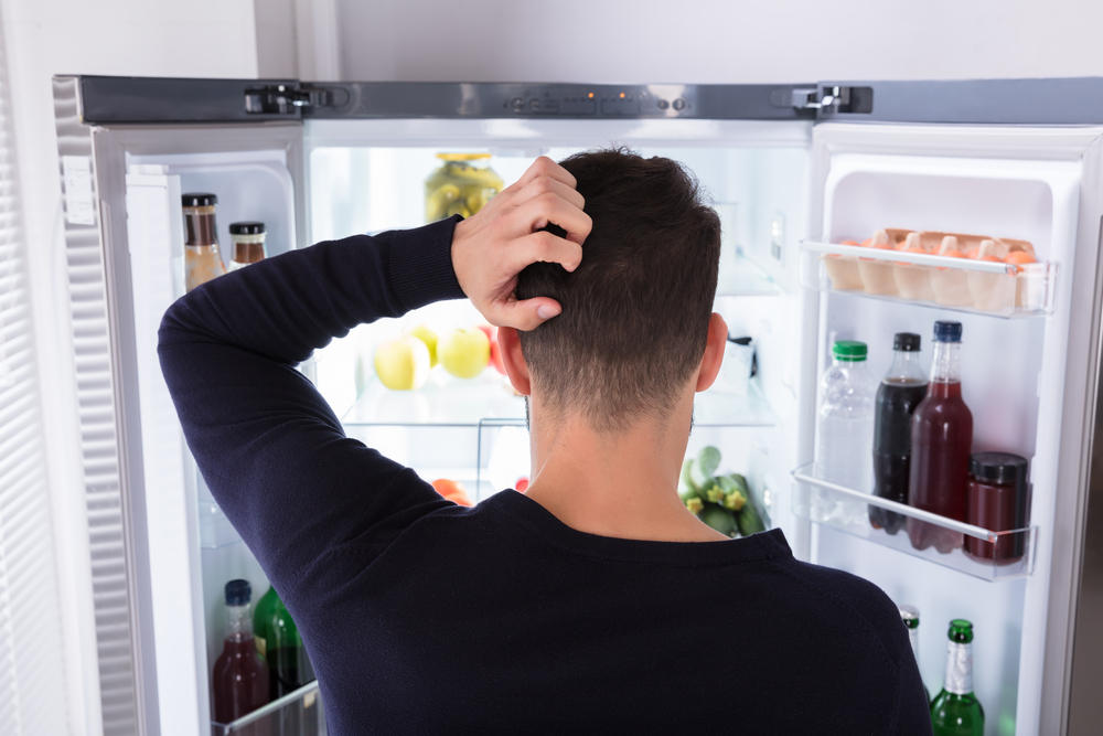 Rear view of a confused man looking at food in refrigerator.