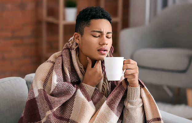 A man holding his throat in pain and drinking a cup of tea.