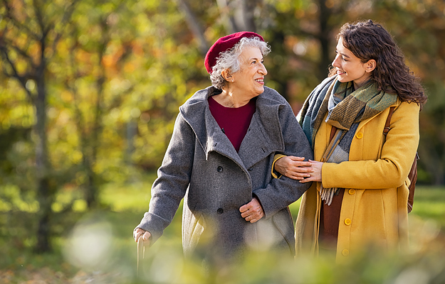 A senior woman and her caregiver walking outside.